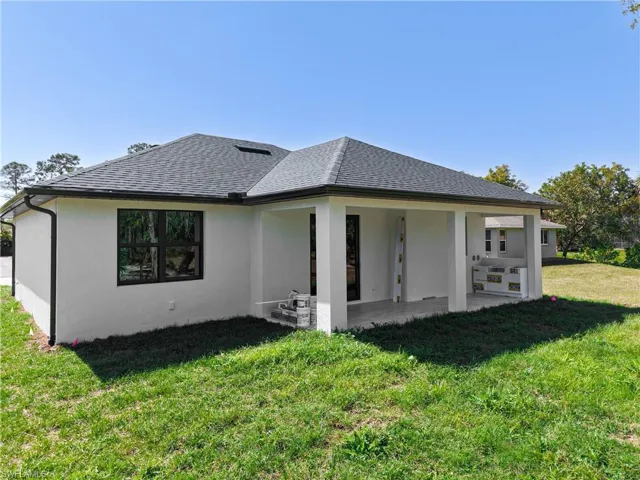 Rear view of house with a patio area, roof with shingles, a yard, and stucco siding