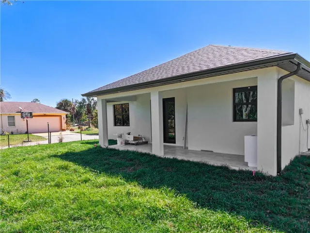Back of property with a shingled roof, a lawn, a patio area, and stucco siding