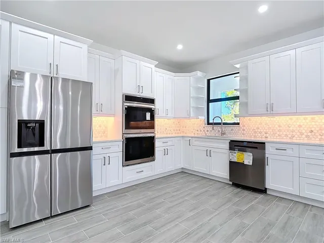 Kitchen featuring open shelves, light countertops, backsplash, appliances with stainless steel finishes, and a sink