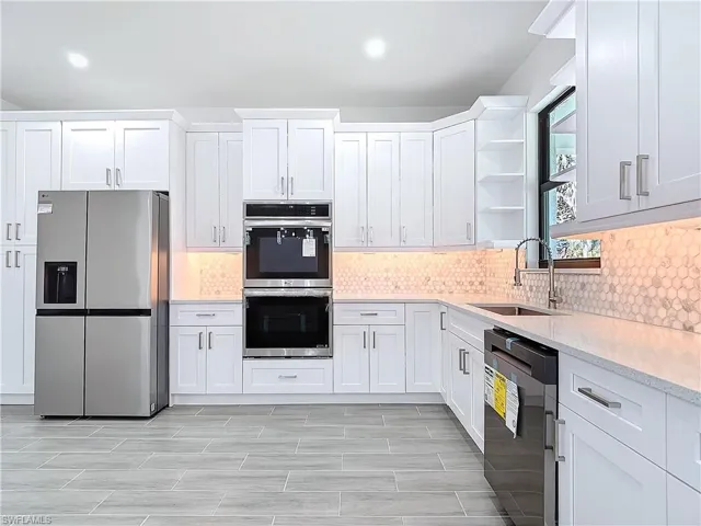 Kitchen featuring open shelves, stainless steel appliances, light countertops, white cabinets, and a sink