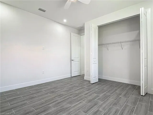 Unfurnished bedroom with wood finish floors, a closet, visible vents, ceiling fan, and baseboards