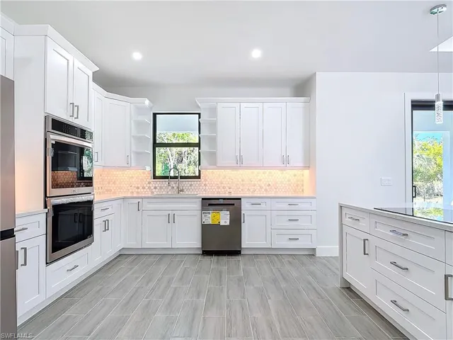 Kitchen with open shelves, light countertops, decorative backsplash, appliances with stainless steel finishes, and a sink