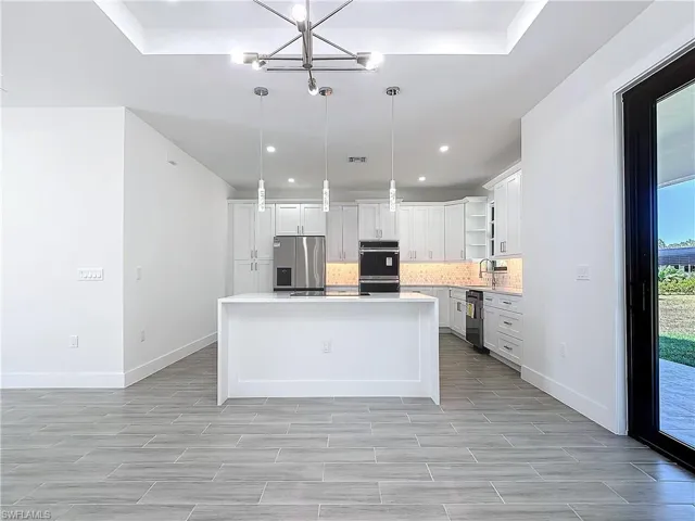 Kitchen with light countertops, decorative backsplash, double oven, a kitchen island, and stainless steel fridge