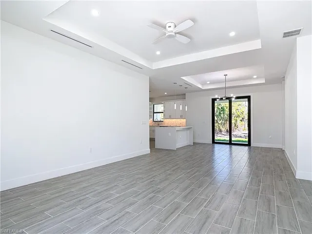 Unfurnished living room featuring recessed lighting, ceiling fan with notable chandelier, visible vents, baseboards, and a raised ceiling