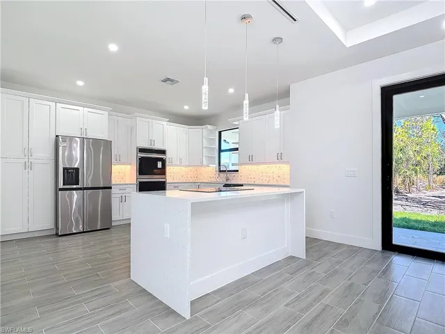 Kitchen with stainless steel appliances, light countertops, visible vents, and backsplash