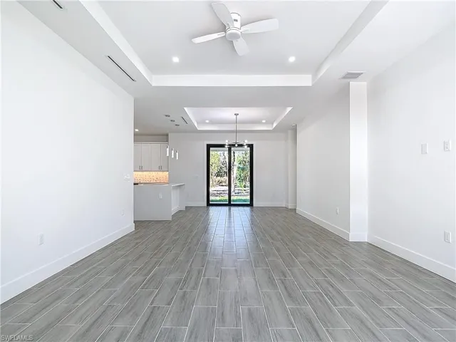 Unfurnished living room featuring visible vents, a tray ceiling, baseboards, and ceiling fan with notable chandelier