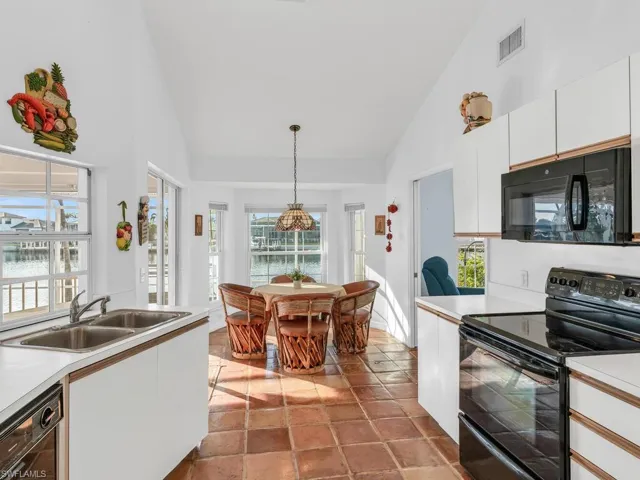Kitchen featuring sink, decorative light fixtures, black appliances, high vaulted ceiling, and white cabinets