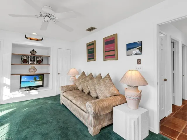 Living room with built in shelves, ceiling fan, and dark colored carpet