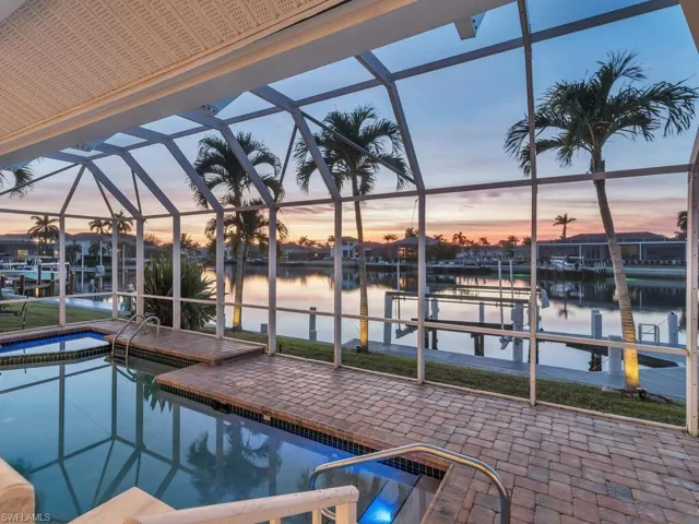 Pool at dusk featuring a water view, a dock, and a lanai