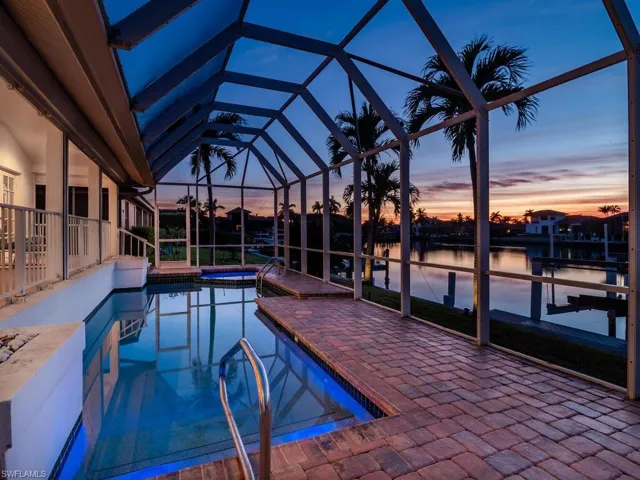 Pool at dusk with a patio, an in ground hot tub, a lanai, a water view, and a dock