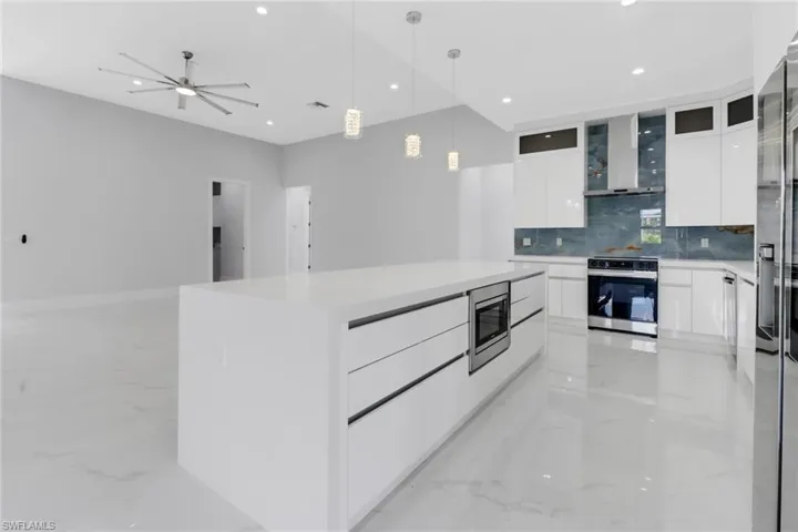 Kitchen featuring ceiling fan, white cabinets, wall chimney exhaust hood, stainless steel appliances, and a center island