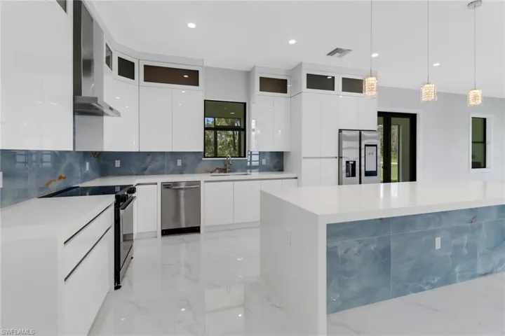 Kitchen with sink, white cabinetry, wall chimney exhaust hood, appliances with stainless steel finishes, and decorative light fixtures