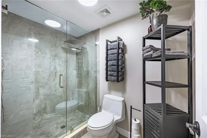 Full glass shower enclosure with floor-to-ceiling marble-look tile, a built-in shower niche, and a rain shower head