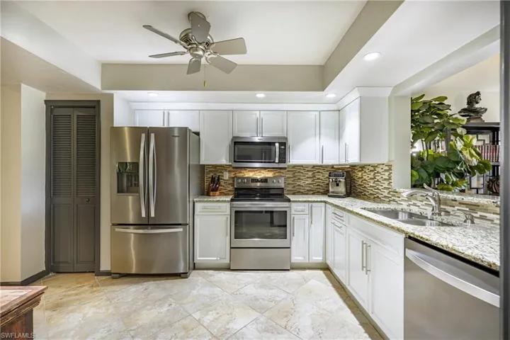 Kitchen featuring white cabinetry, stainless steel appliances, a multi-tone tile backsplash, and light-toned granite countertops