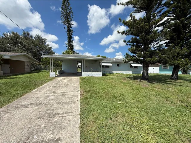 Charming single-story home featuring a covered front carport, expansive manicured lawn, and mature tree-lined landscape
