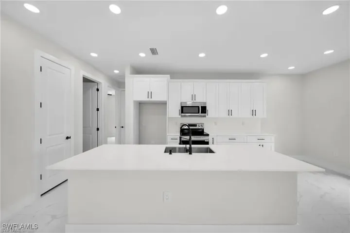 Kitchen with recessed lighting, white cabinets, stainless steel appliances, a center island with sink, and light marble finish flooring