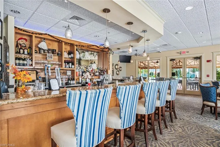 Community bar area with a drop ceiling, pendant lighting, light stone countertops, and french doors