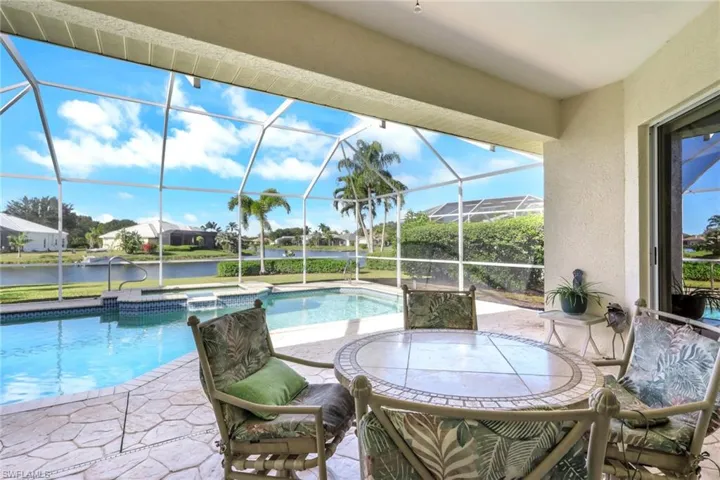 View of pool featuring a sunroom, a patio, a water view, glass enclosure, and a pool with connected hot tub
