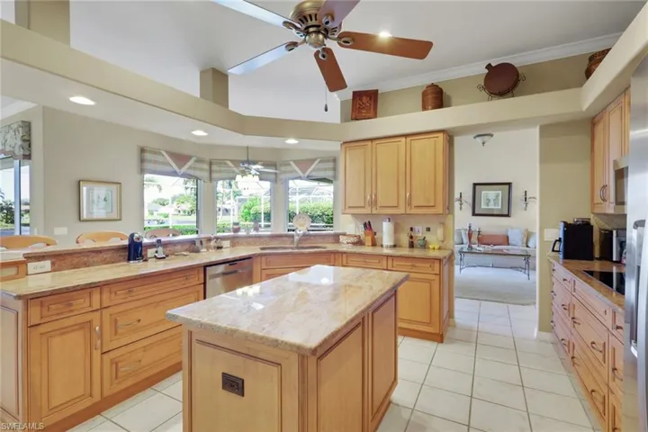 Kitchen with a peninsula, light stone countertops, light tile patterned floors, a ceiling fan, and ornamental molding