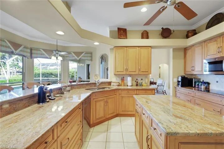 Kitchen featuring a ceiling fan, crown molding, light stone counters, stainless steel appliances, and a center island