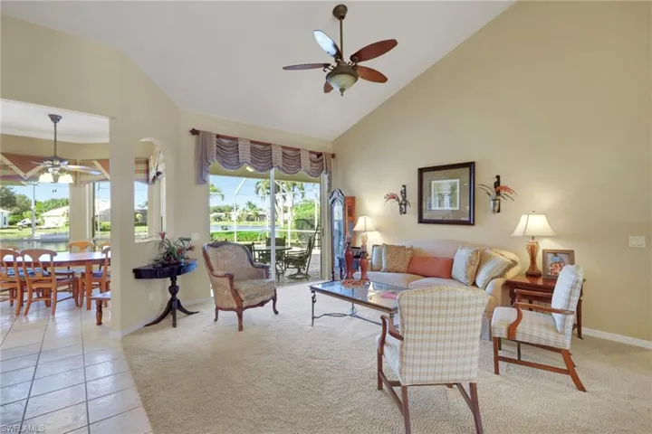 Living room with ceiling fan, high vaulted ceiling, light carpet, and light tile patterned flooring