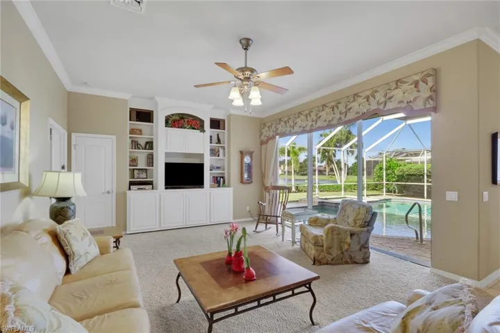 Carpeted living area with a sunroom, ornamental molding, ceiling fan, and built in features