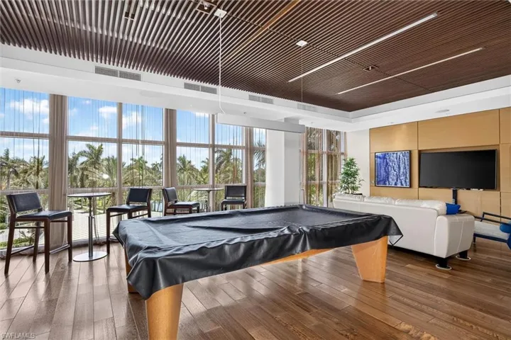 Expansive room featuring wood-finish flooring, a wood slat ceiling with integrated lighting, a wall of floor-to-ceiling windows, and a built-in media wall