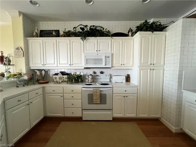 Kitchen with white appliances, white cabinets, Corian Countertops,  Hardwood finished floors, and Cove Moldings