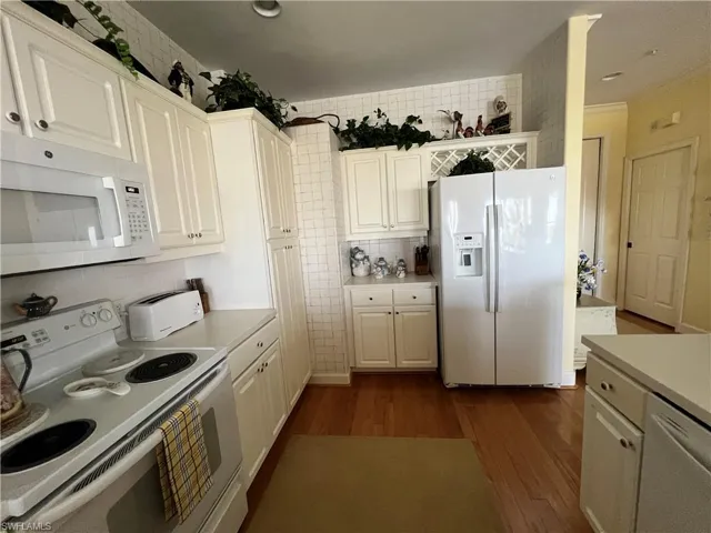 Kitchen with white appliances, white cabinets, Corian Counter-tops, Hardwood finished floors, and Cove Moldings and decorative back-splash