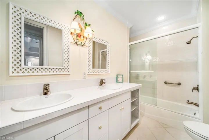 Full bathroom featuring shower / bath combination with glass door, dual bowl vanity, toilet, tile patterned floors, and ornamental molding