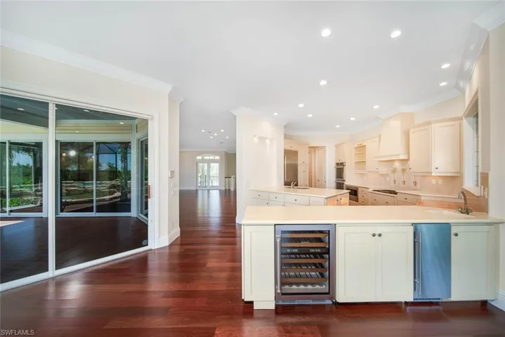 Kitchen featuring tasteful backsplash, wine cooler, kitchen peninsula, premium range hood, and dark hardwood / wood-style flooring