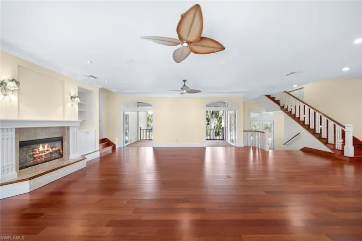 Unfurnished living room with a tiled fireplace, built in shelves, ceiling fan, and hardwood / wood-style floors