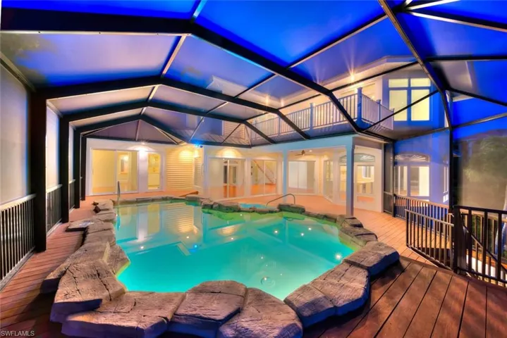 View of pool with a deck, glass enclosure, and a hot tub