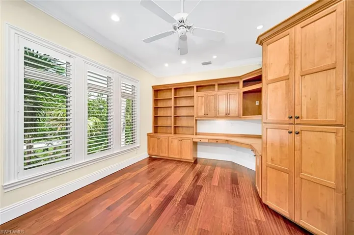 Unfurnished office with dark wood-type flooring, built in desk, ornamental molding, and ceiling fan