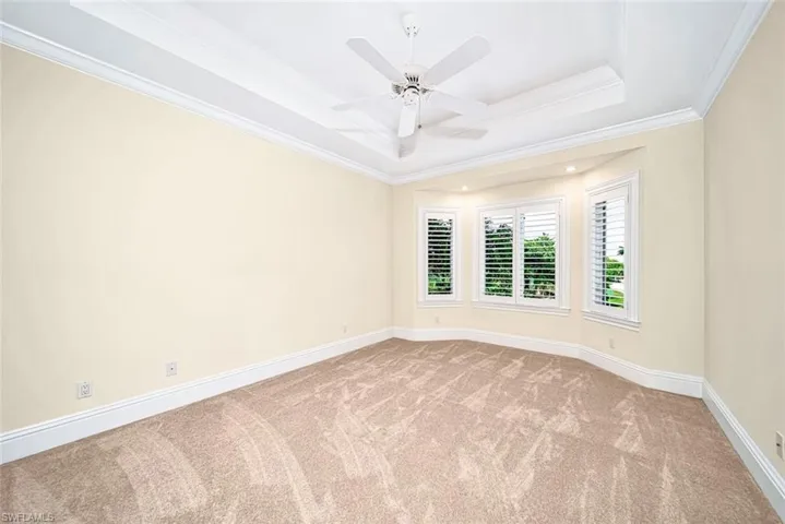 Empty room featuring ornamental molding, carpet flooring, ceiling fan, and a raised ceiling