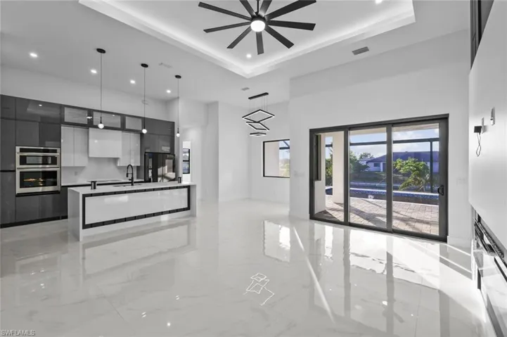 Kitchen featuring multiple ovens, a tray ceiling, ceiling fan, decorative light fixtures, and a kitchen island
