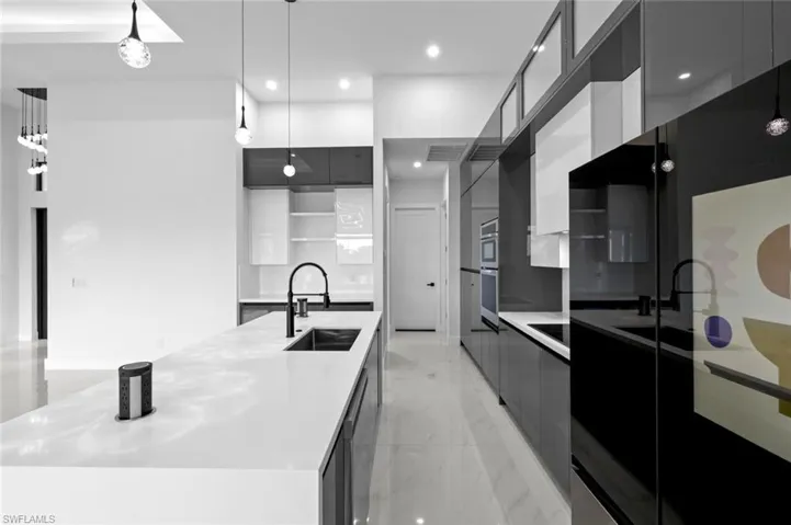 Kitchen with stainless steel double oven, a spacious island, sink, pendant lighting, and a high ceiling