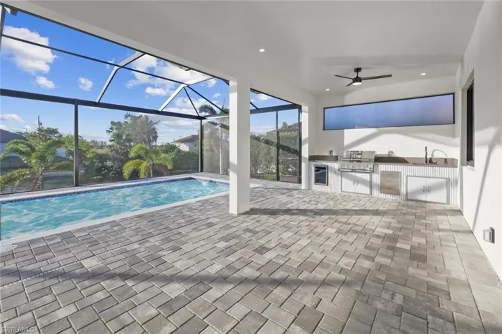 View of pool with sink, an outdoor kitchen, a lanai, a grill, and a patio area