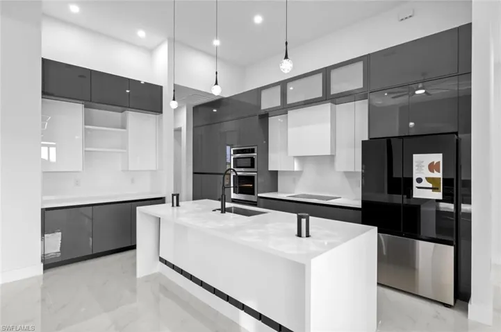 Kitchen with stainless steel appliances, a kitchen island with sink, sink, white cabinetry, and hanging light fixtures