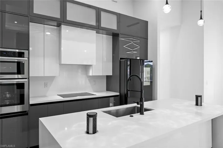 Kitchen with black electric stovetop, stainless steel double oven, sink, pendant lighting, and white cabinets