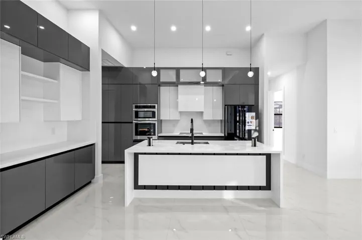Kitchen with a large island, sink, stainless steel double oven, black fridge, and decorative light fixtures