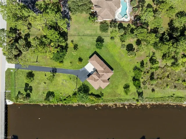 Waterfront property featuring a modern residence with distinctive peaked roofing, situated on expansive grounds with mature landscaping, manicured lawn, and direct water access along the shoreline