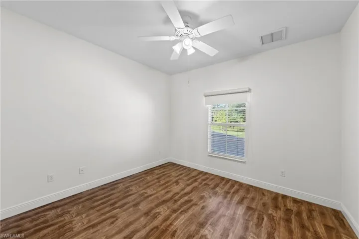 Wood-finish flooring, white walls, window with roller shade, and a ceiling fan with light fixture