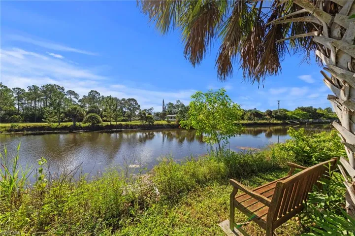 Waterfront setting with lush green banks, mature trees, and a wooden bench