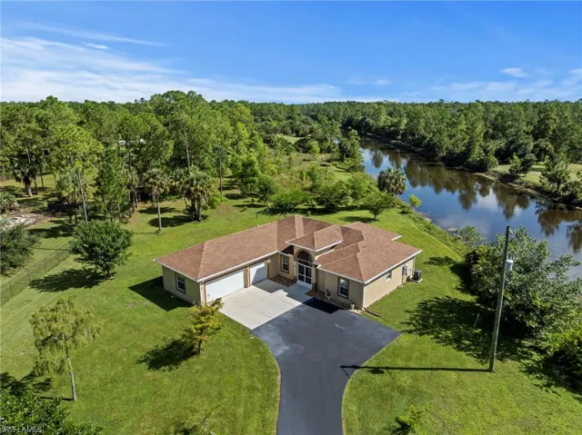 Waterfront property featuring a private paved driveway, an attached garage, and a lush green lawn
