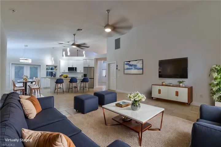 Living room featuring ceiling fan with notable chandelier, baseboards, visible vents, and stone tile floors