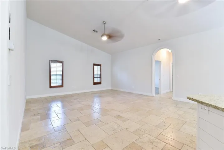 Spare room featuring arched walkways, stone tile floors, baseboards, and ceiling fan