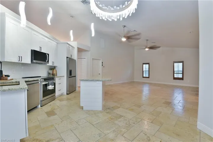 Kitchen with ceiling fan, high vaulted ceiling, stone tile floors, a kitchen island, and stainless steel appliances