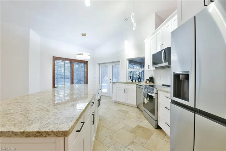 Kitchen featuring white cabinetry, light stone countertops, appliances with stainless steel finishes, stone tile floors, and a sink
