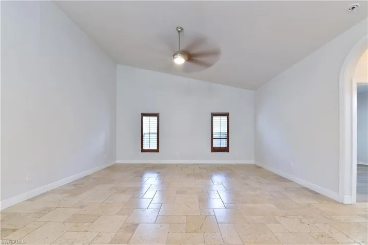 Spare room featuring baseboards, a ceiling fan, high vaulted ceiling, arched walkways, and stone tile floors